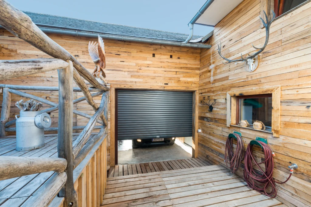 Houten garage met grijze rolpoort, rustieke balustrade en decoratieve wandaccessoires. | Zonwering.nl