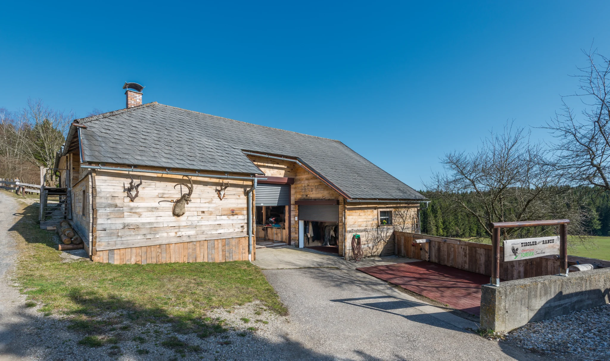 Houten ranchgebouw met twee grijze rolpoorten in een landelijke omgeving. | Zonwering.nl