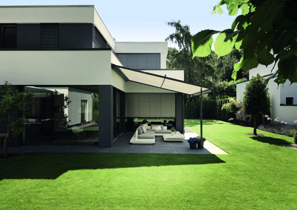 Moderne woning met pergolazonwering boven een loungeset en buitenjaloezieën aan de gevel. | Zonwering .nl
