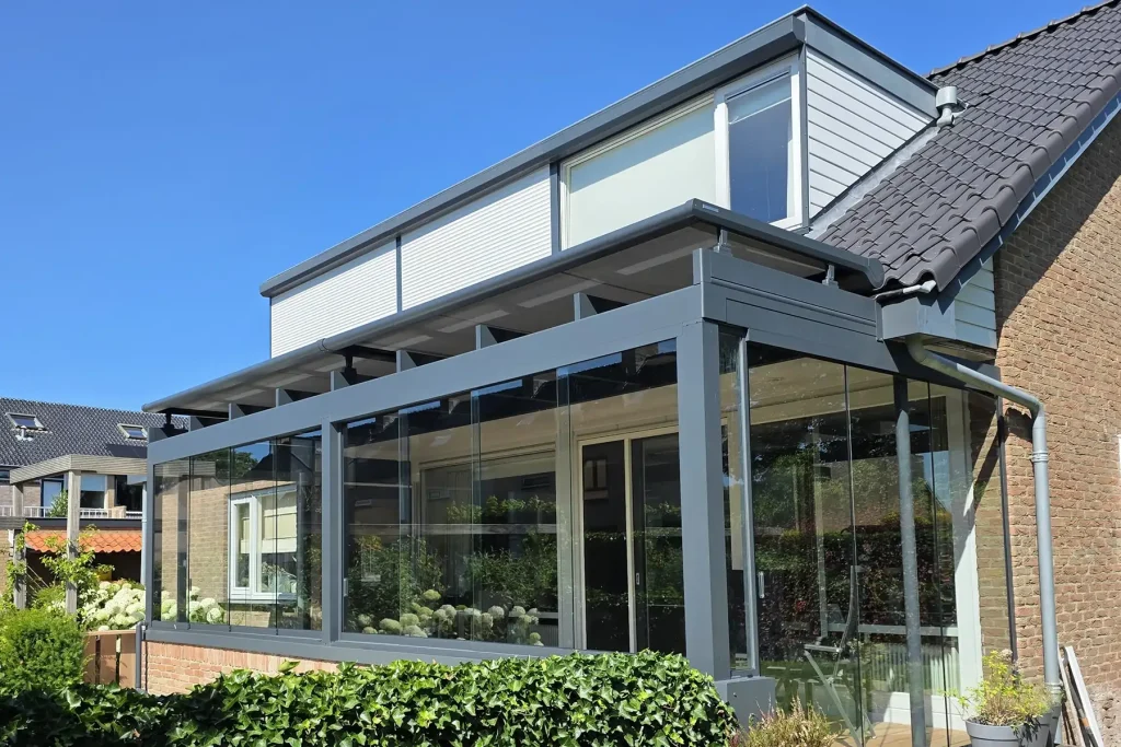 Glazen veranda met grijze aluminium constructie en geïntegreerde zonwering aan een woning.